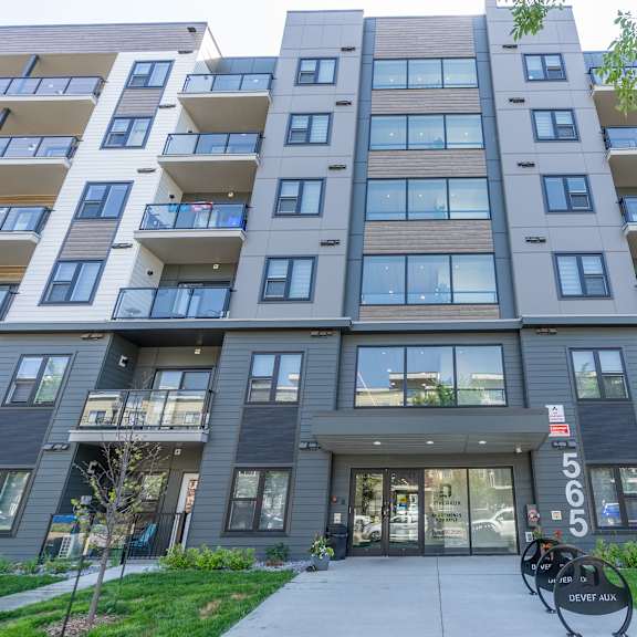 the image shows a modern apartment building with a grey and white exterior and a glass entrance.