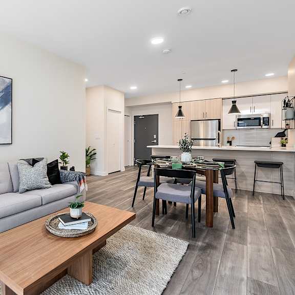 a modern living room with a grey sofa, a wooden coffee table, and a dining area in the background.