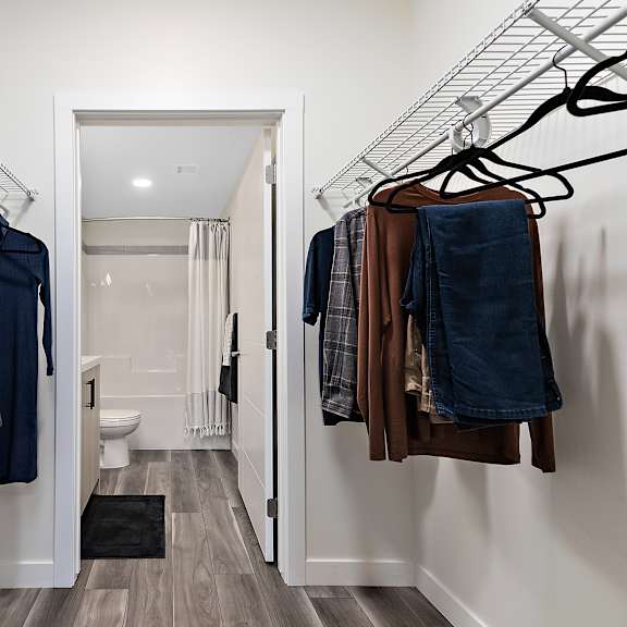 a hallway with clothes hanging on racks and a toilet in the background.