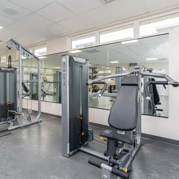 a gym with a variety of equipment including treadmills, stationary bikes, and weight machines. at g17 apartments at tamarack, edmonton, alberta