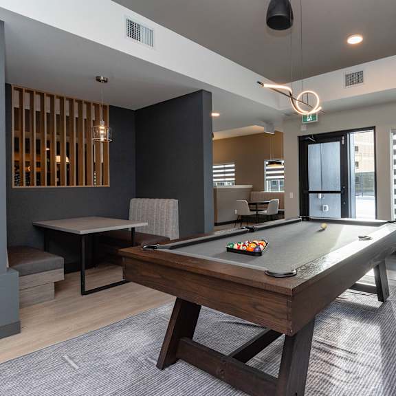 a pool table is in the middle of a room with a chair and a bar stool.at vibe apartments at arbour lake, alberta