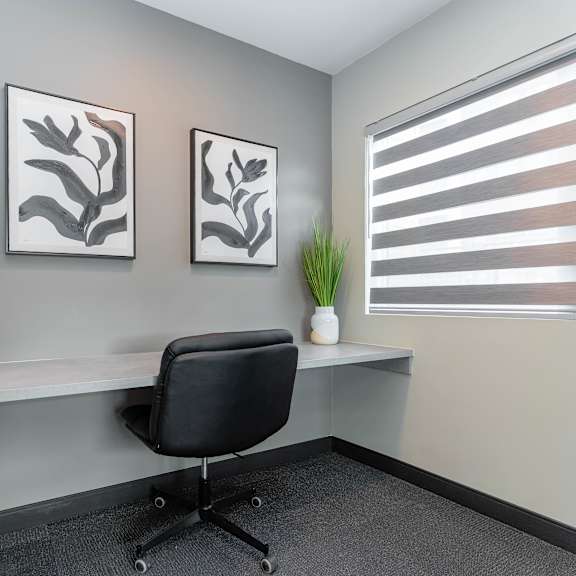 a black chair is in front of a desk with two framed pictures on the wall.at vibe apartments at arbour lake, calgary