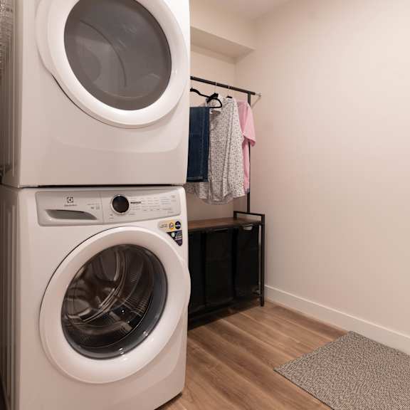 a white front loading washing machine is stacked on top of another one in a laundry room.at vibe apartments at arbour lake, calgary, ab