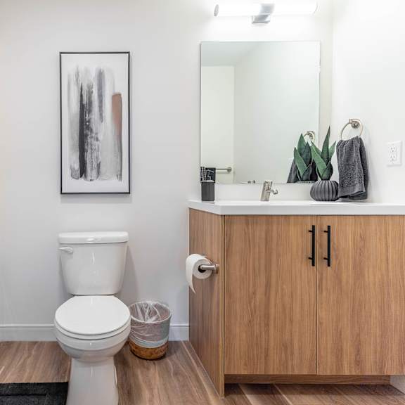 a white toilet sits in a bathroom next to a wooden cabinet.at vibe apartments at arbour lake, calgary, ab t3g 4j2