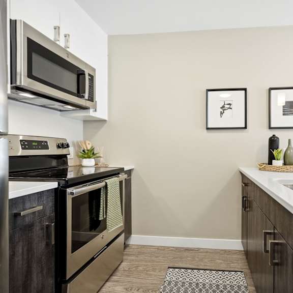 a kitchen with a stainless steel refrigerator and oven, a microwave above the stove, and a sink with a basket of fruit on the counter.