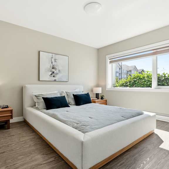 a bedroom with a large bed, a nightstand with a lamp, and a window with a view of the outside.