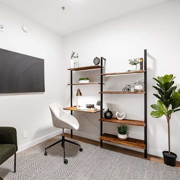 a room with a green couch, a blackboard, a desk, a chair, a shelf with plants and decorations, and a potted plant.