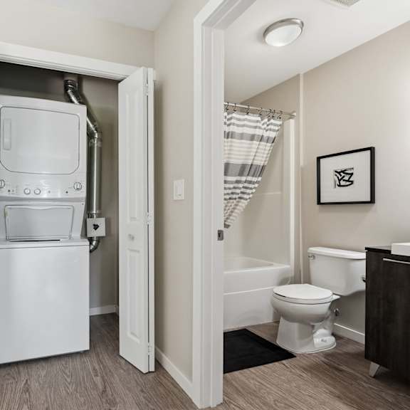 a white refrigerator is in the middle of a room with a toilet and a bathtub in the background.