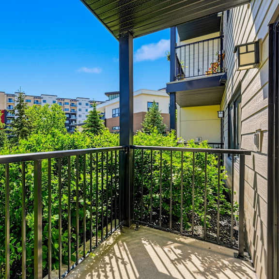 a balcony with a metal railing overlooks a green lawn and apartment buildings.