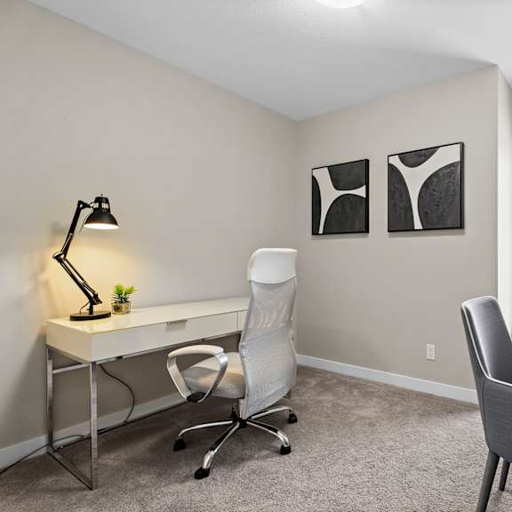a room with a desk, chair, and two framed pictures on the wall.