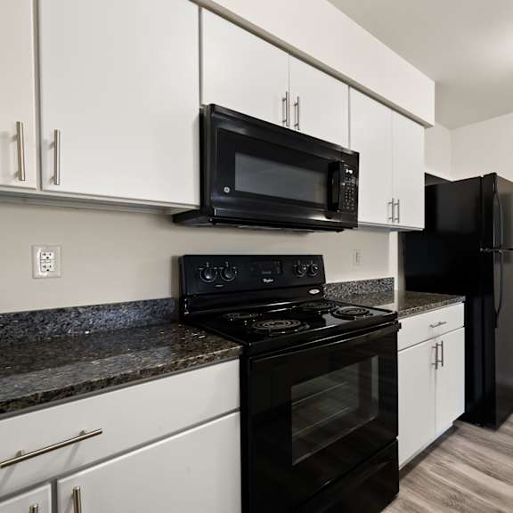 a black microwave is mounted above a black refrigerator in a kitchen.