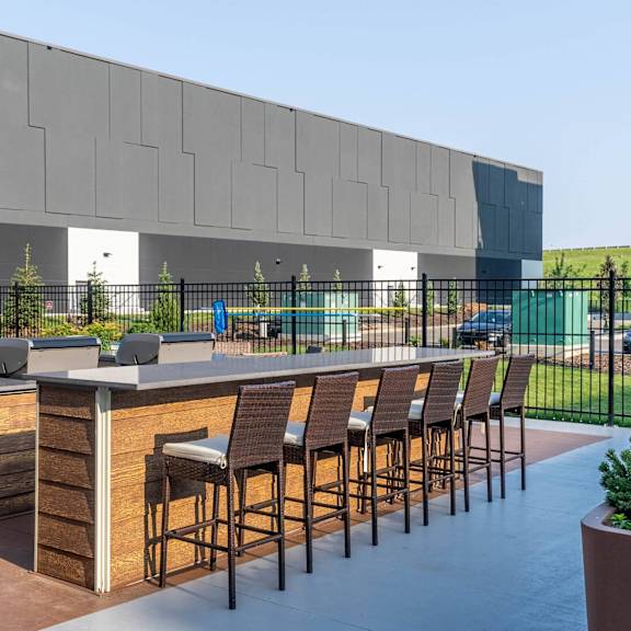 a modern outdoor bar area with wooden stools and a counter. at g17 apartments at tamarack, edmonton, ab