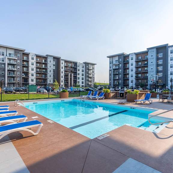 a swimming pool surrounded by sun loungers and chairs in front of apartment buildings. at g17 apartments at tamarack, edmonton, ab