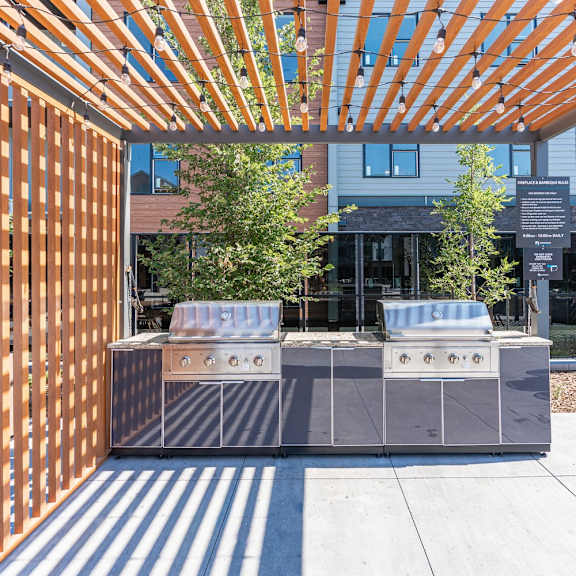 a modern outdoor kitchen with a grill and a wooden pergola.