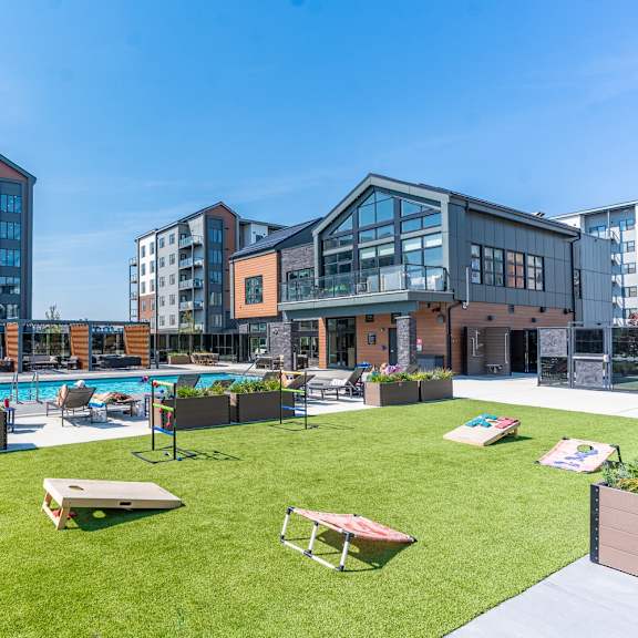 a large grassy area with a pool and sun loungers in front of apartment buildings.