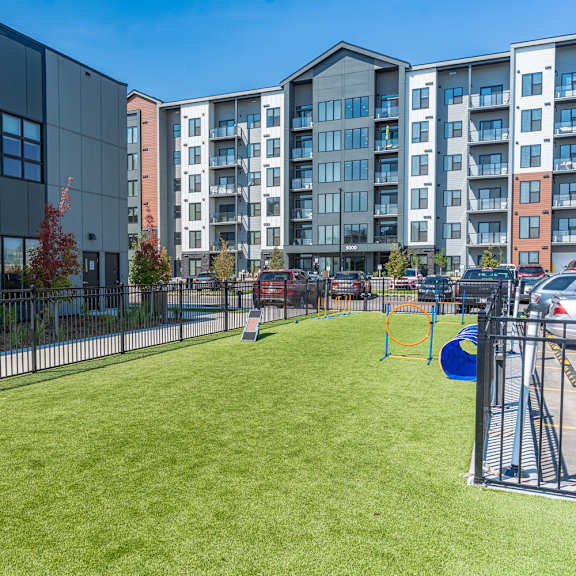 a playground with a slide and swings is surrounded by a fence and a grassy area in front of a building.