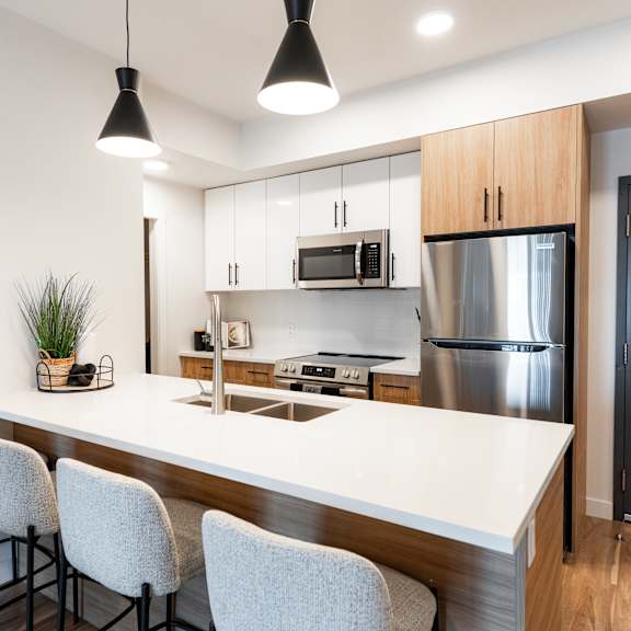a modern kitchen with a bar area and chairs.at podium apartments, calgary, ab