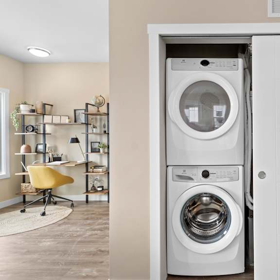 a white washing machine is in a white cabinet in a room with a yellow chair.