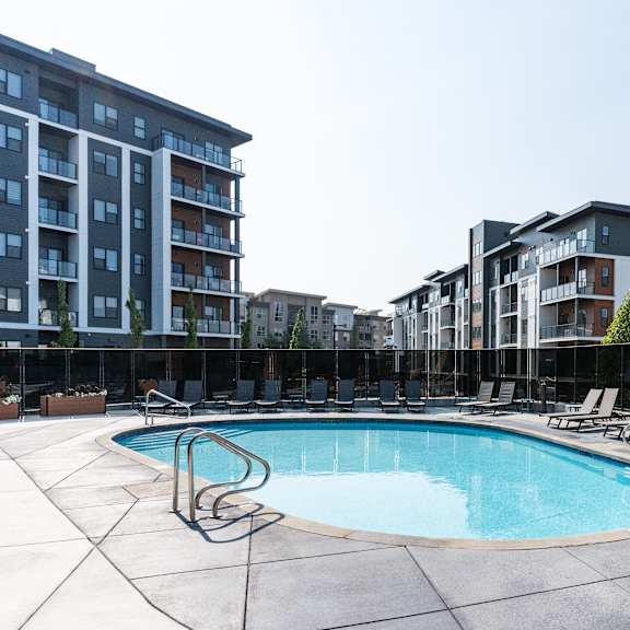 a swimming pool surrounded by lounge chairs and apartment buildings. at vibe apartments at arbour lake, alberta