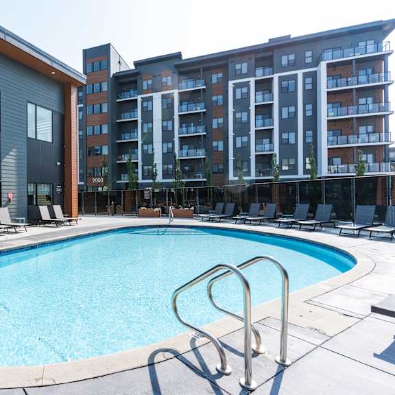 a swimming pool with a metal ladder in front of a building. at vibe apartments at arbour lake, alberta