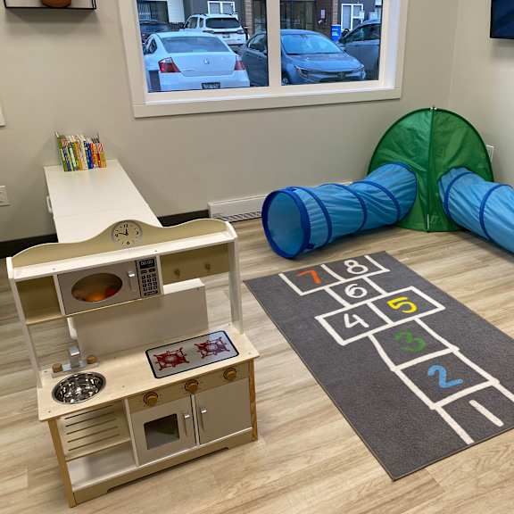 a child's play area with a wooden play kitchen, a tunnel, and a mat with numbers.