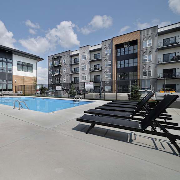 a swimming pool area with sun loungers and a building in the background.