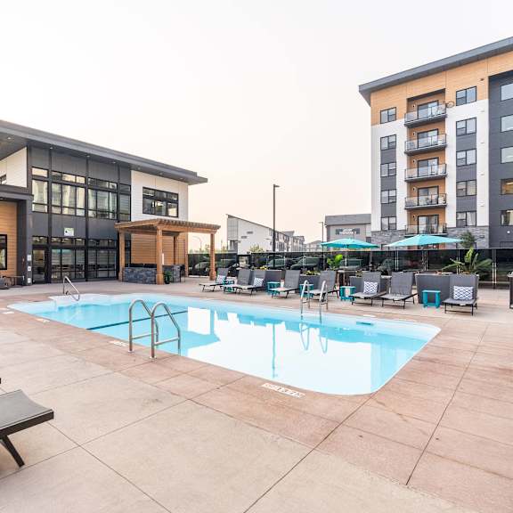 a pool area with sun loungers and a building in the background.