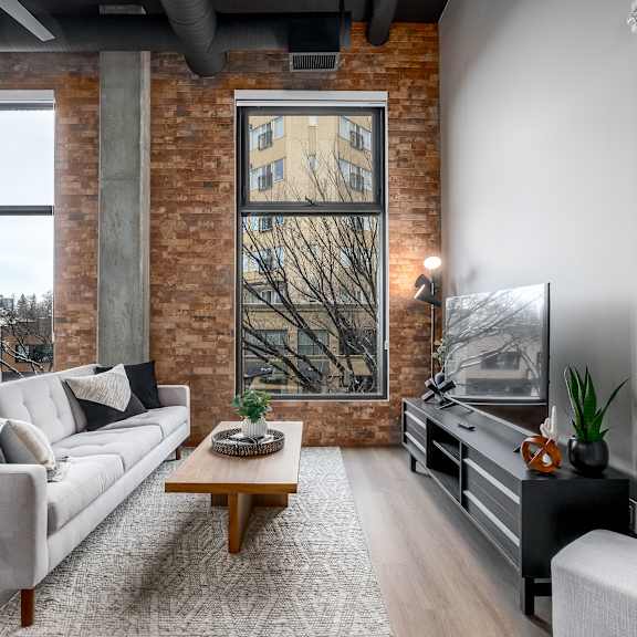 a living room with a grey couch, a wooden coffee table, and a large window with a view of a tree.at raymond block, edmonton alberta t6e 3r7