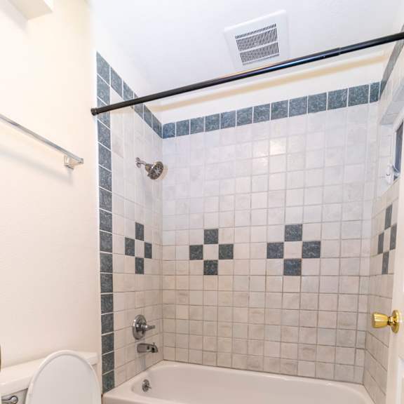 a white toilet is in a bathroom with a white bathtub and a black and white tile shower.