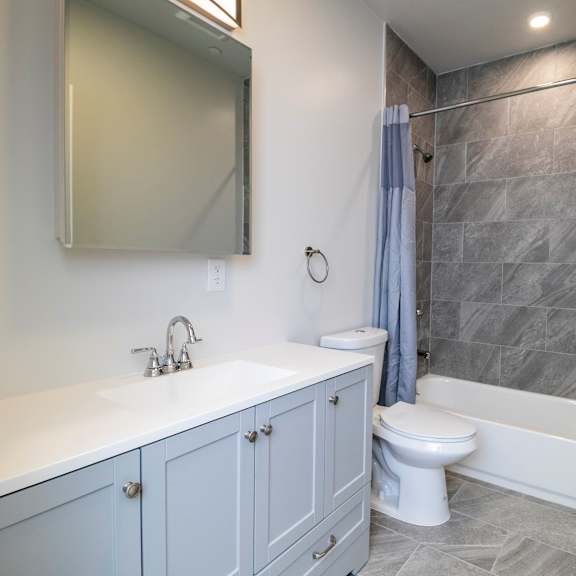 a bathroom with a white sink, grey cabinets, and a grey tiled shower.