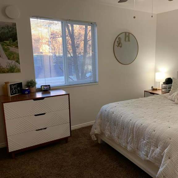 a bedroom with a bed, nightstand, and a window with blinds.