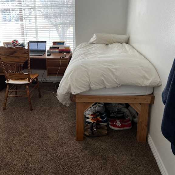 a bedroom with a bed, desk, chair, and shoes.