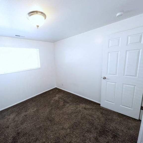 a room with a carpeted floor, a white door, and a window with blinds.