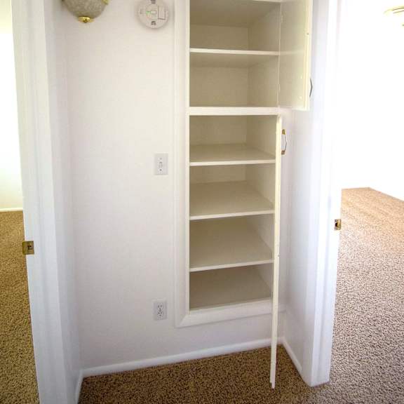 a white closet with a carpeted floor and a light on the wall.