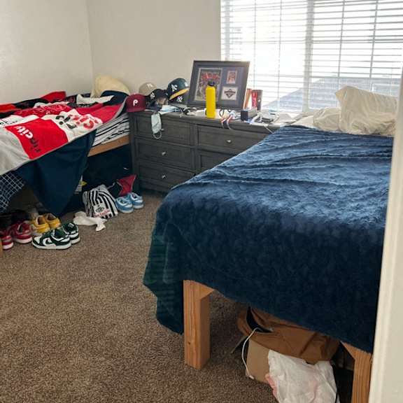 a bedroom with a bed, dresser, and window with blinds.