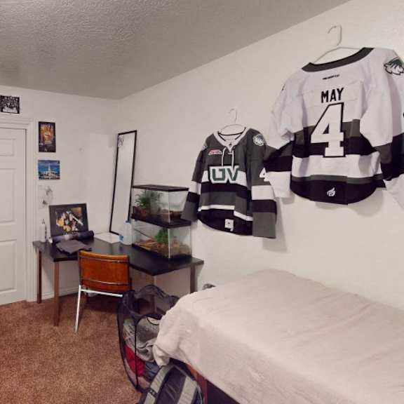 a room with a bed, a chair, a desk, and a hockey jersey hanging on the wall.