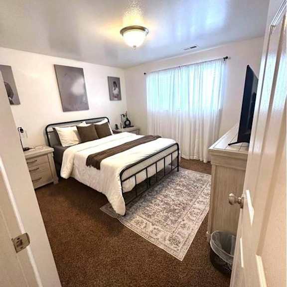 a bedroom with a bed, nightstand, and window with curtains.