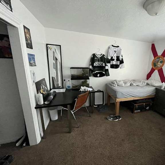 a room with a bed, desk, and a ceiling fan.