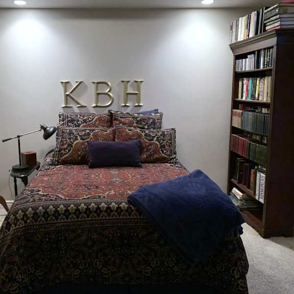 a bedroom with a bed, a bookshelf, and a wall with the letters "kbh" on it.