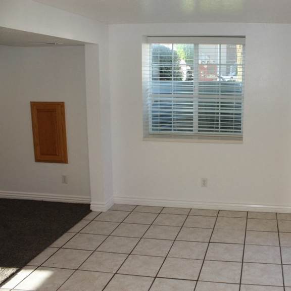 a room with a white door, a window with blinds, and a tiled floor.