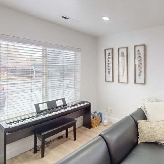 a black leather couch sits in a living room with a piano and two framed pictures on the wall.