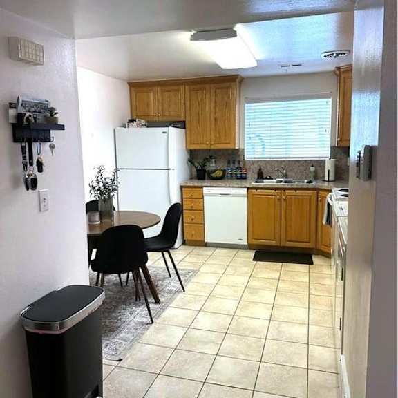 a kitchen with a white refrigerator, black chairs, and a black trash can.