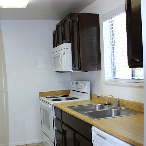 a small kitchen with a white dishwasher and a white microwave above the stove.