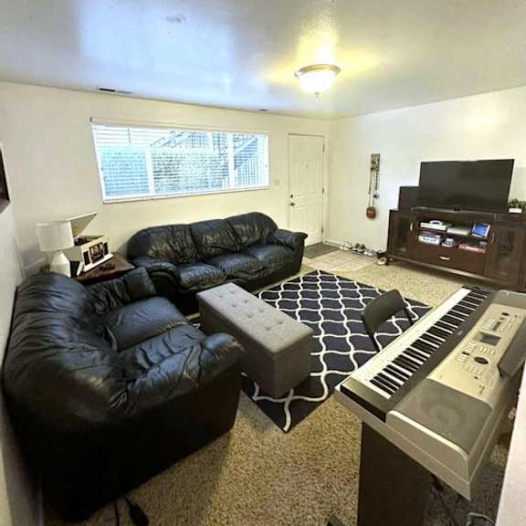 a black leather couch sits in a living room with a piano in the corner.