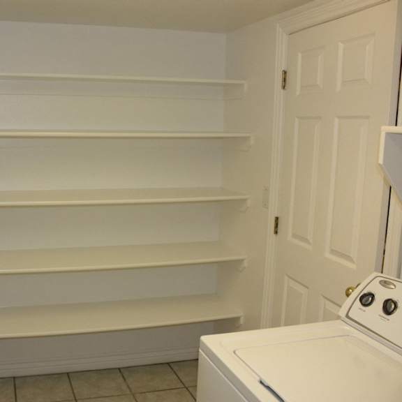 a white washing machine sits in a laundry room with a white door and shelves.