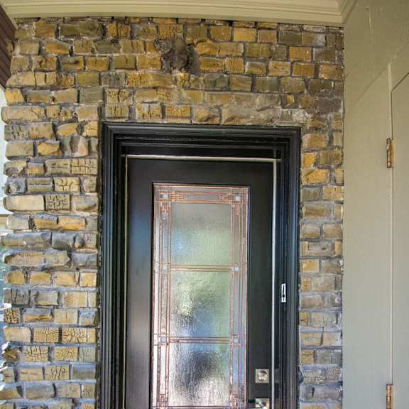 a black door with a glass window is set in a brick wall.