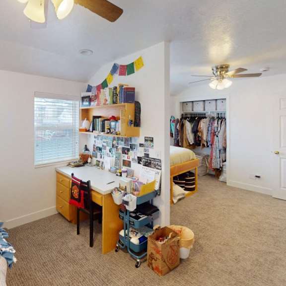 a bedroom with a bed, desk, and a fan.
