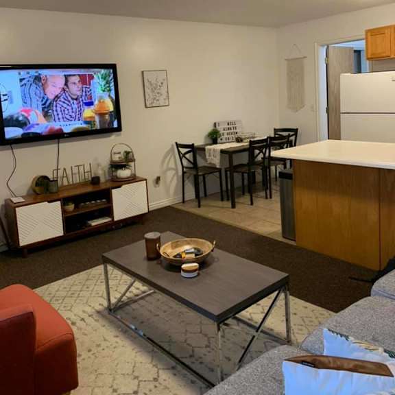 a living room with a television on the wall and a dining table with chairs.