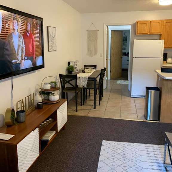 a kitchen with a refrigerator, a dining table with chairs, and a tv mounted on the wall.