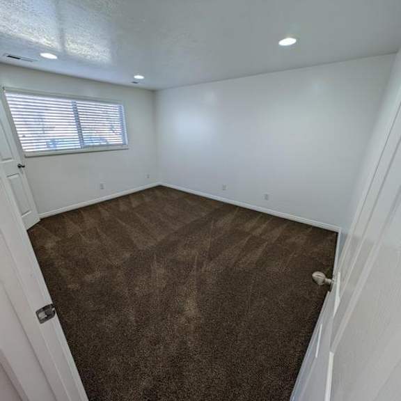 a room with brown carpet and a window with blinds.